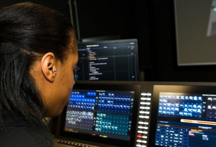 Young woman in dark room looking at a bank of screens showing data